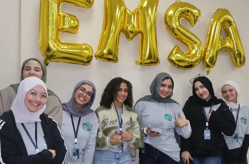 Seven EMSA-BUC members in grey uniform smiling under gold EMSA balloon letters at the First Union