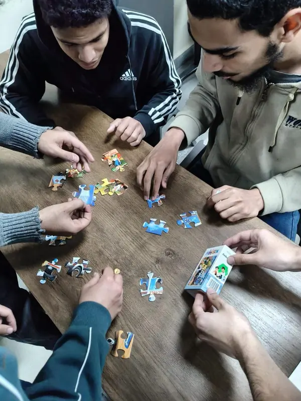 Several pairs of hands assemble a jigsaw puzzle together on a desk